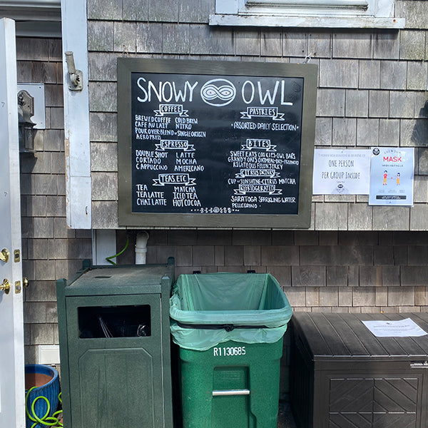 Extensive specialty coffee menu board featuring freshly roasted espresso drinks, artisanal lattes, and unique house-crafted beverages at Snowy Owl Coffee, displayed on a rustic cedar-shingled wall.
